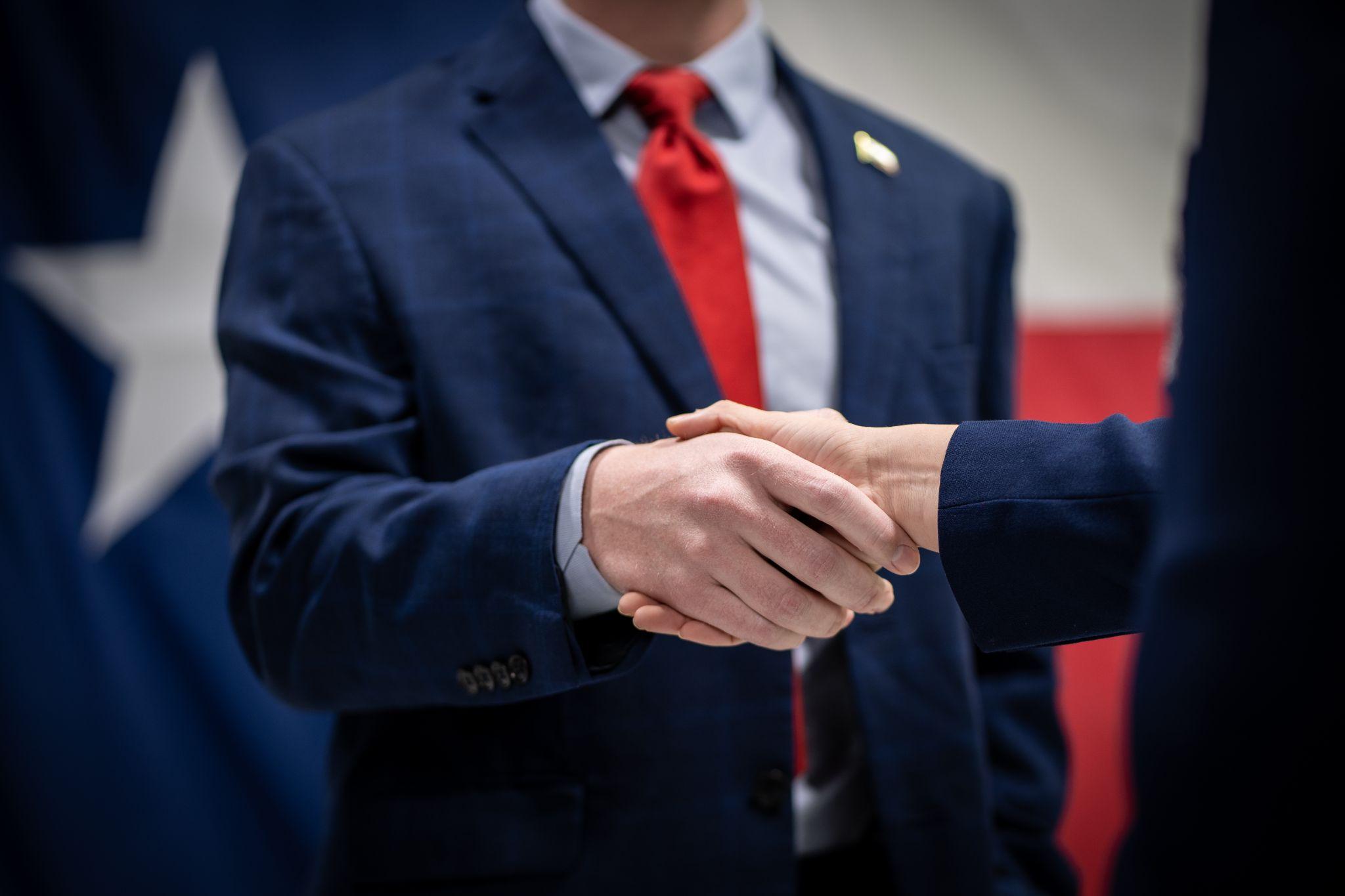 Male and Female Business Professionals or Politicians In Suits Shaking Hands In Front of Flag Close Up.