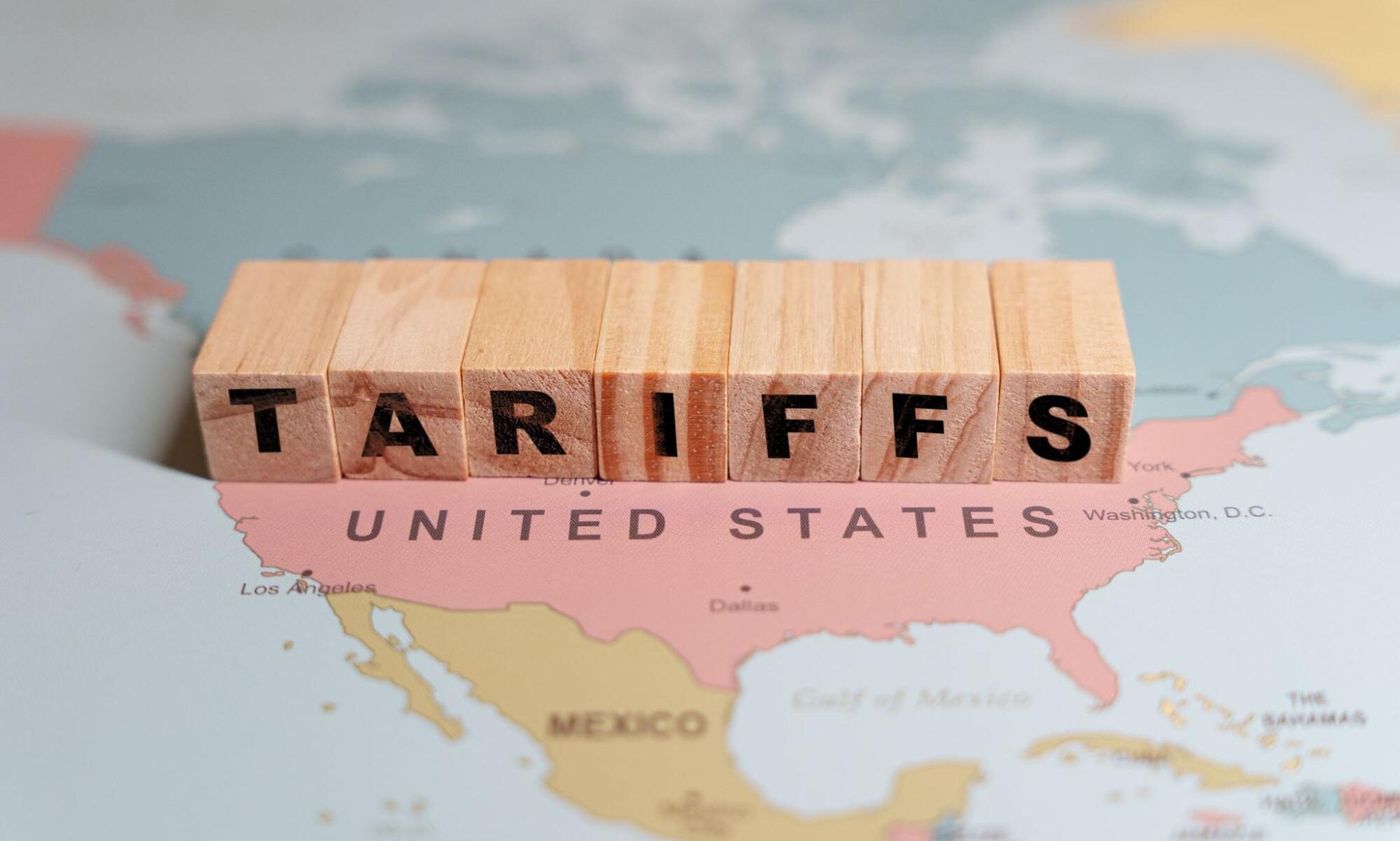 Wooden blocks spelling TARIFFS are placed on a map of North America, specifically over the United States and Mexico.