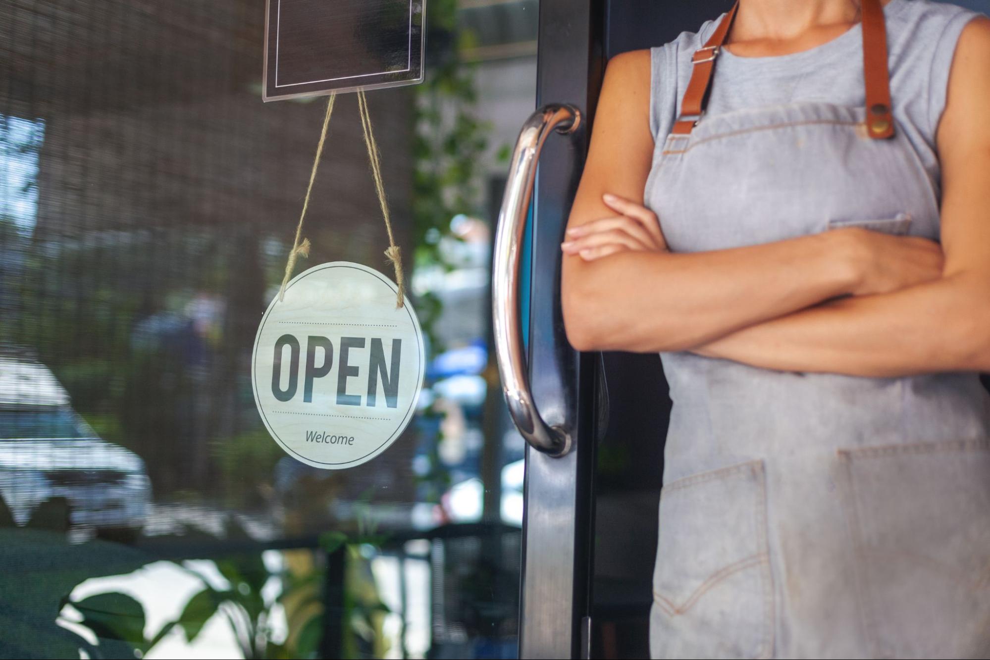 The woman is a waitress in an apron, the owner of the cafe stands at the door with a sign Open waiting for customers.