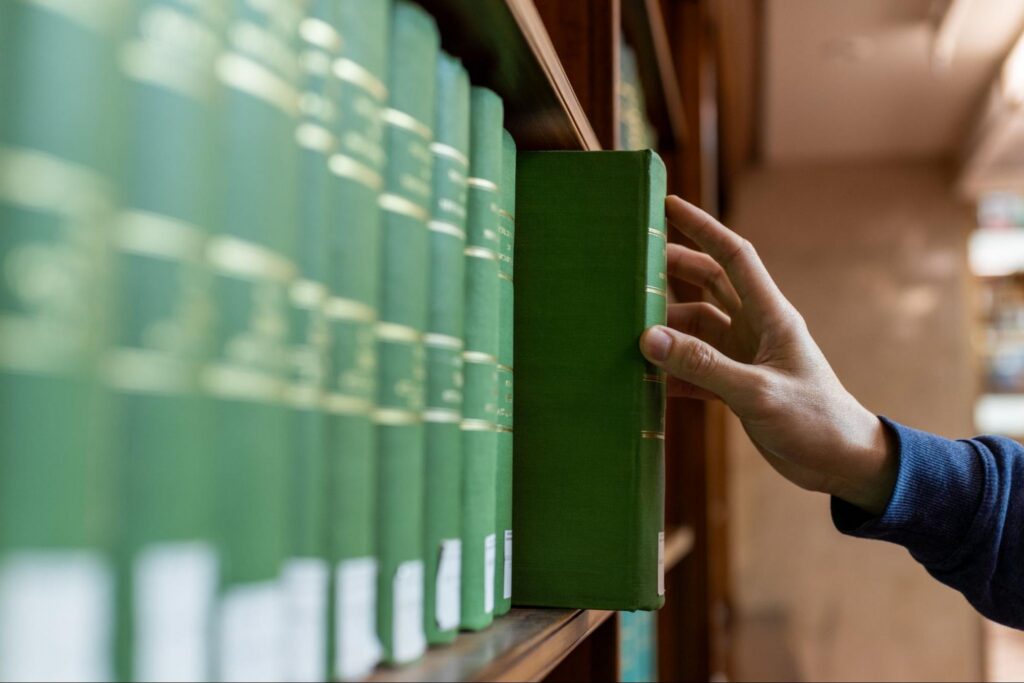 Hand selecting book from wooden library shelf.